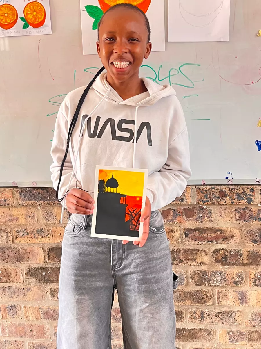 A smiling young person holding up a small painted artwork