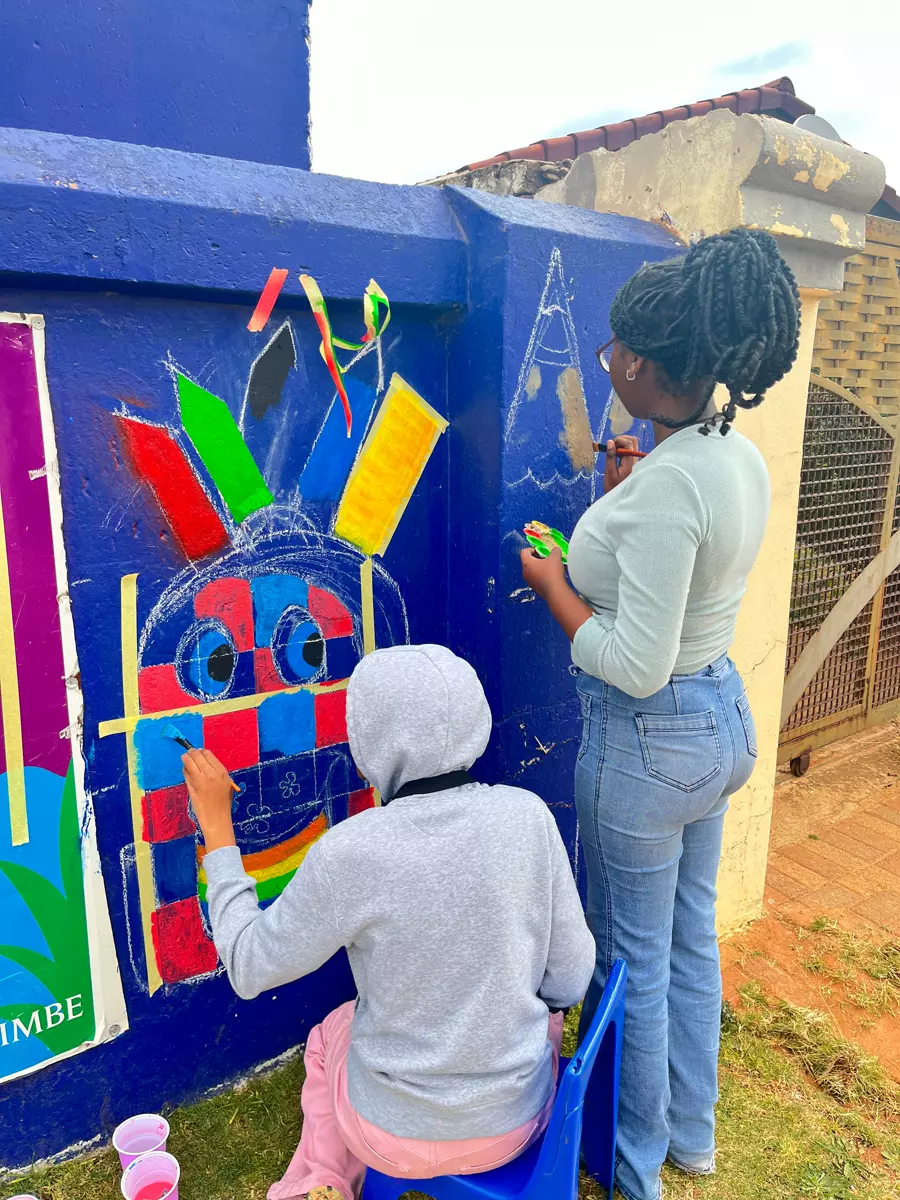 Two young women painting a blue wall outdoors