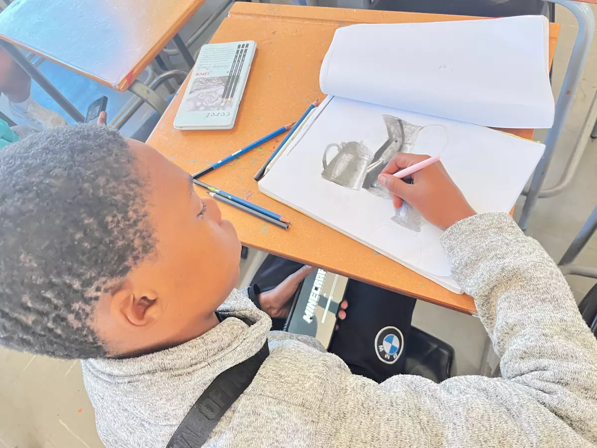 A young boy drawing in a sketchbook at a school desk