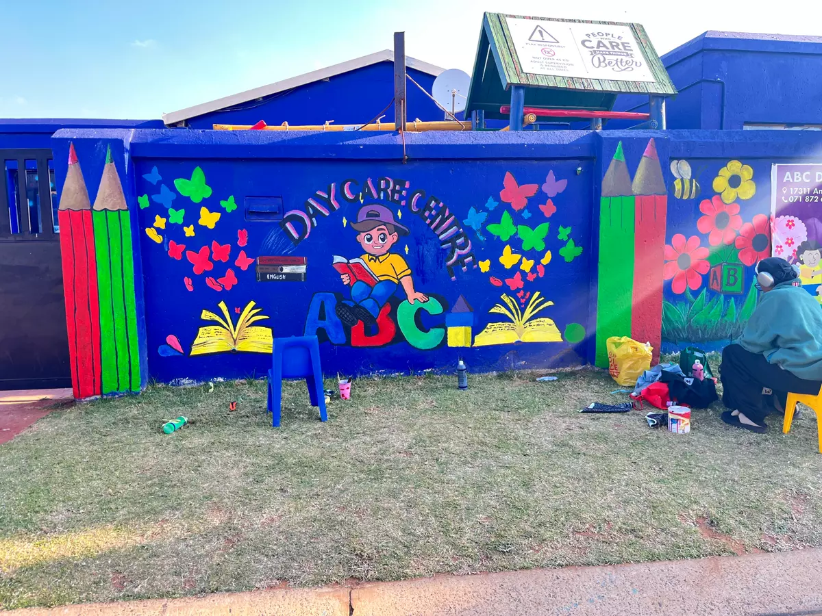 A vibrant daycare centre mural on a blue wall with a person sitting nearby