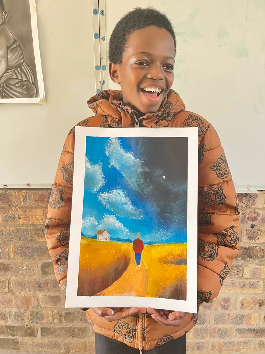 A smiling boy holding up a painting he created of a landscape with a lone figure