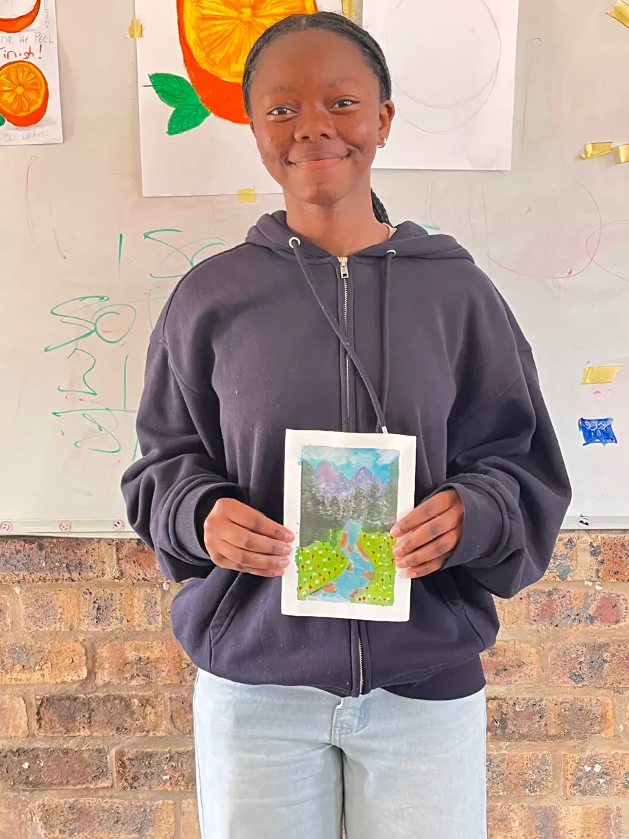 A young woman holding up a small painted landscape artwork