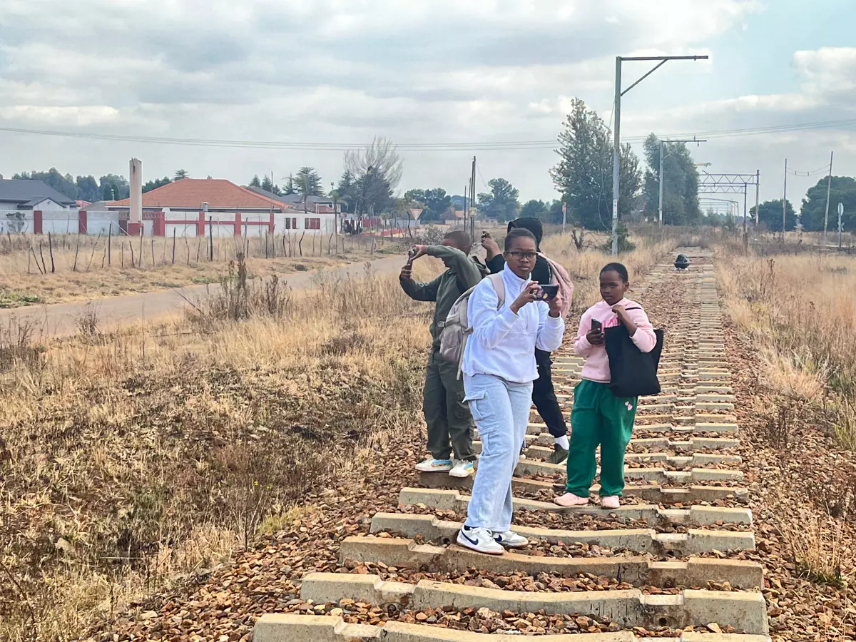 Four people standing on a railroad track taking pictures in a grassy field