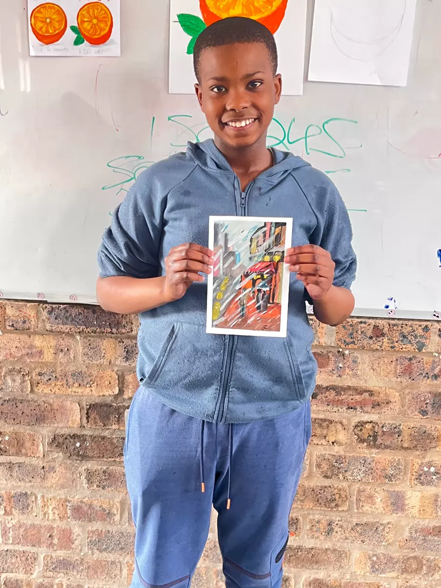 A young person holding up a small painting in front of a whiteboard