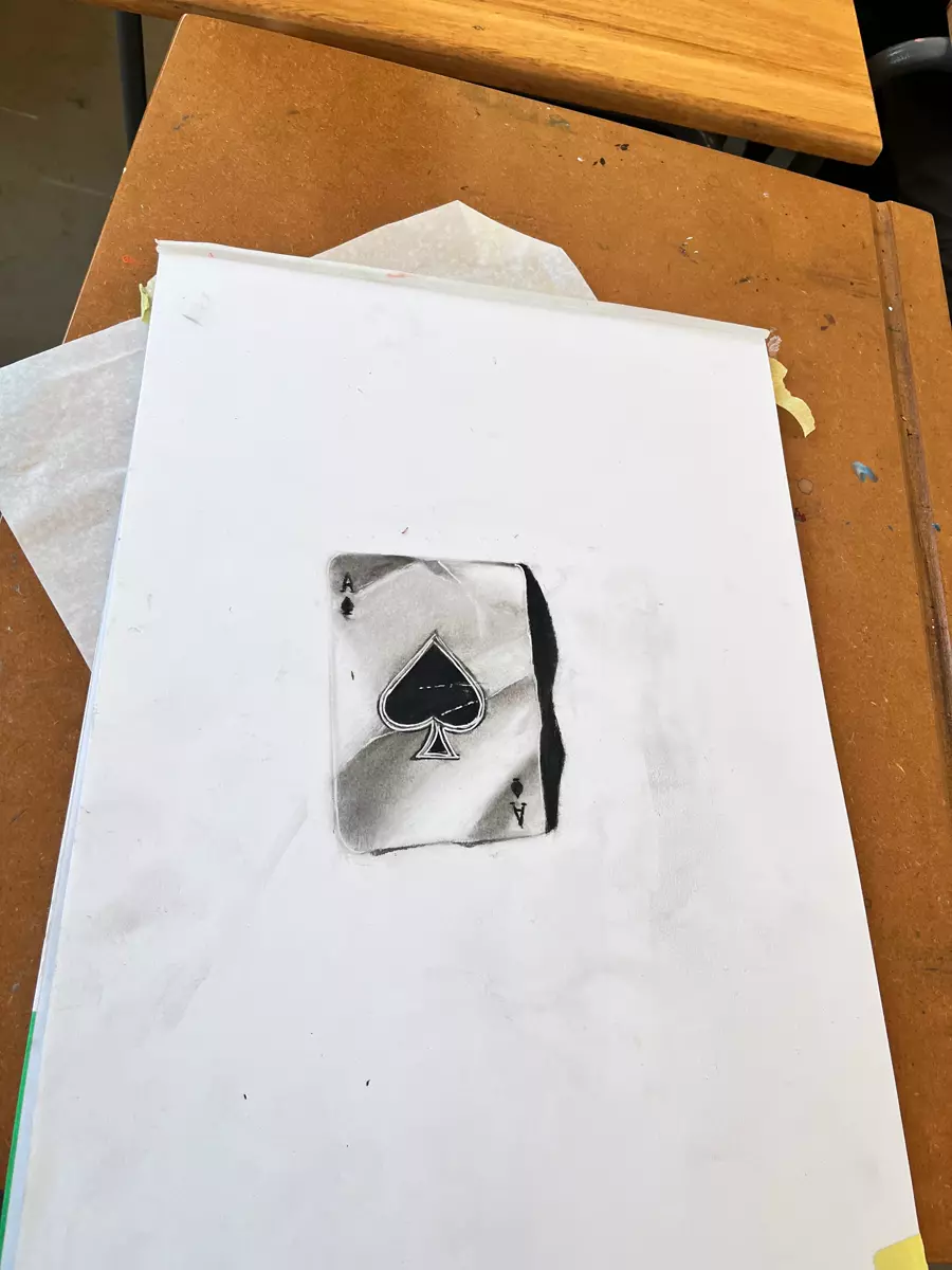 A charcoal drawing of an ace of spades card on paper on a wooden table