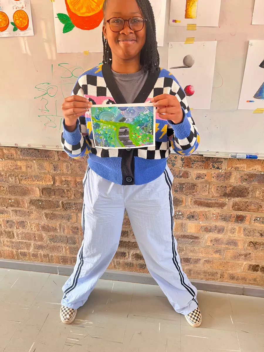 A young woman smiling while holding up her colourful painting