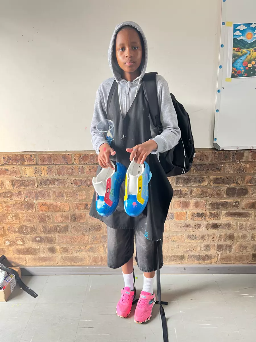 A young artist holding up a pair of custom painted shoes