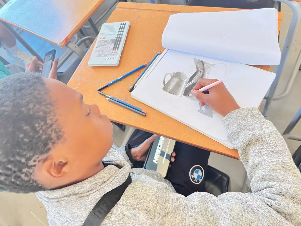 A young boy drawing in a notebook at a school desk